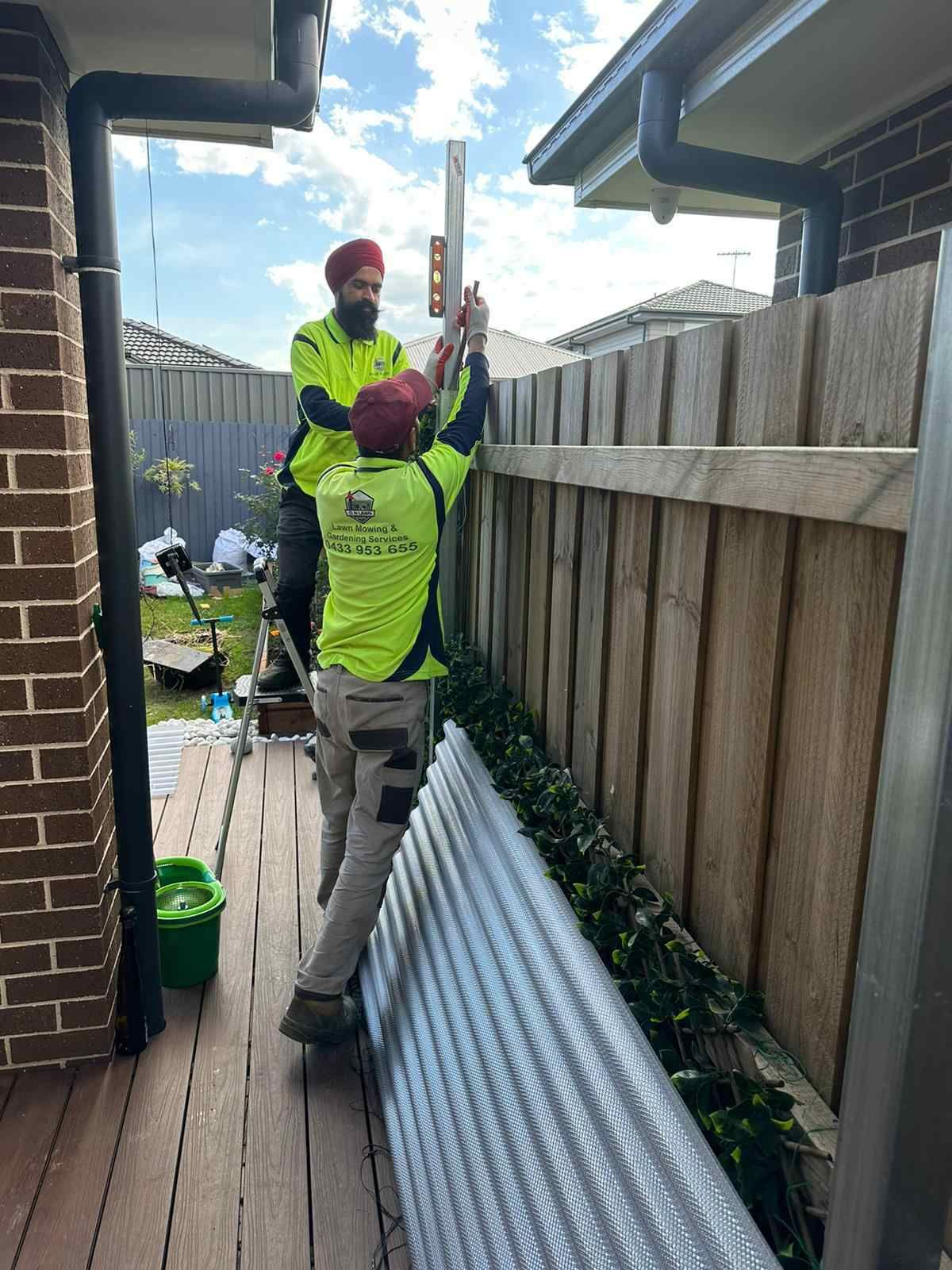 Two men are working on a wooden fence in front of a house.