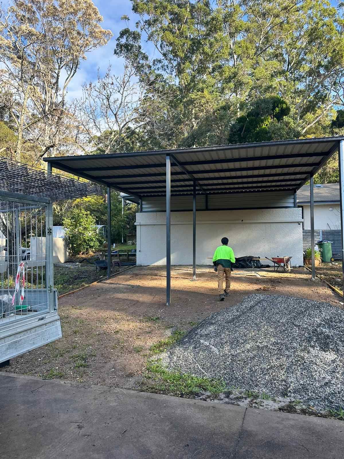 A man in a green vest is standing in front of a carport.