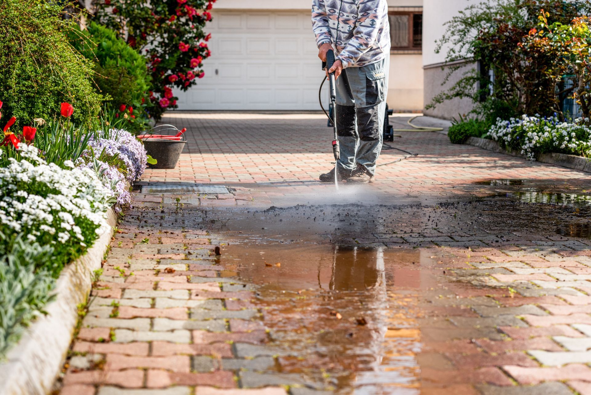A man is cleaning a brick driveway with a high pressure washer.