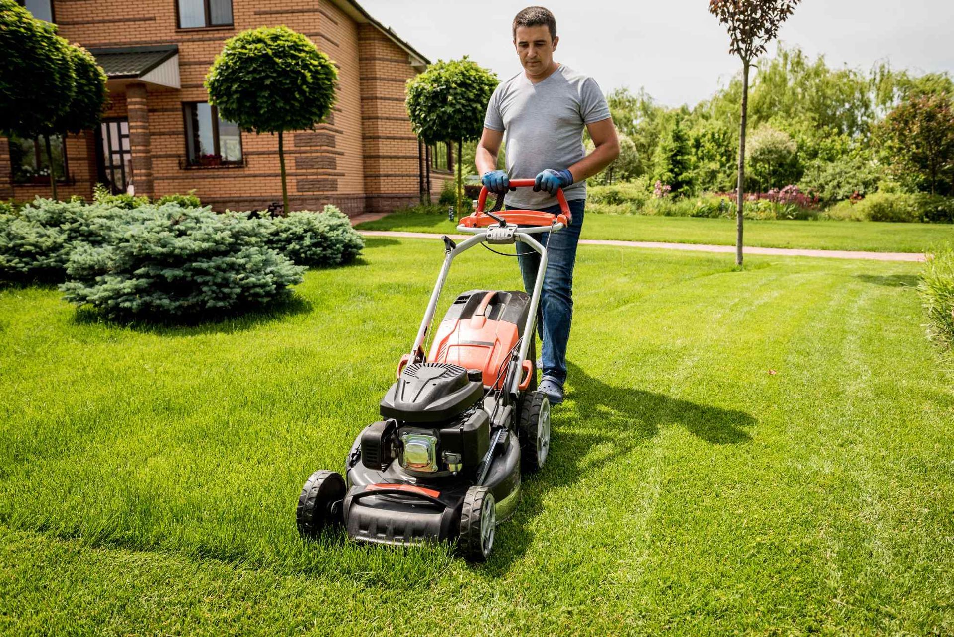 A man is using a lawn mower to cut the grass in front of a house.