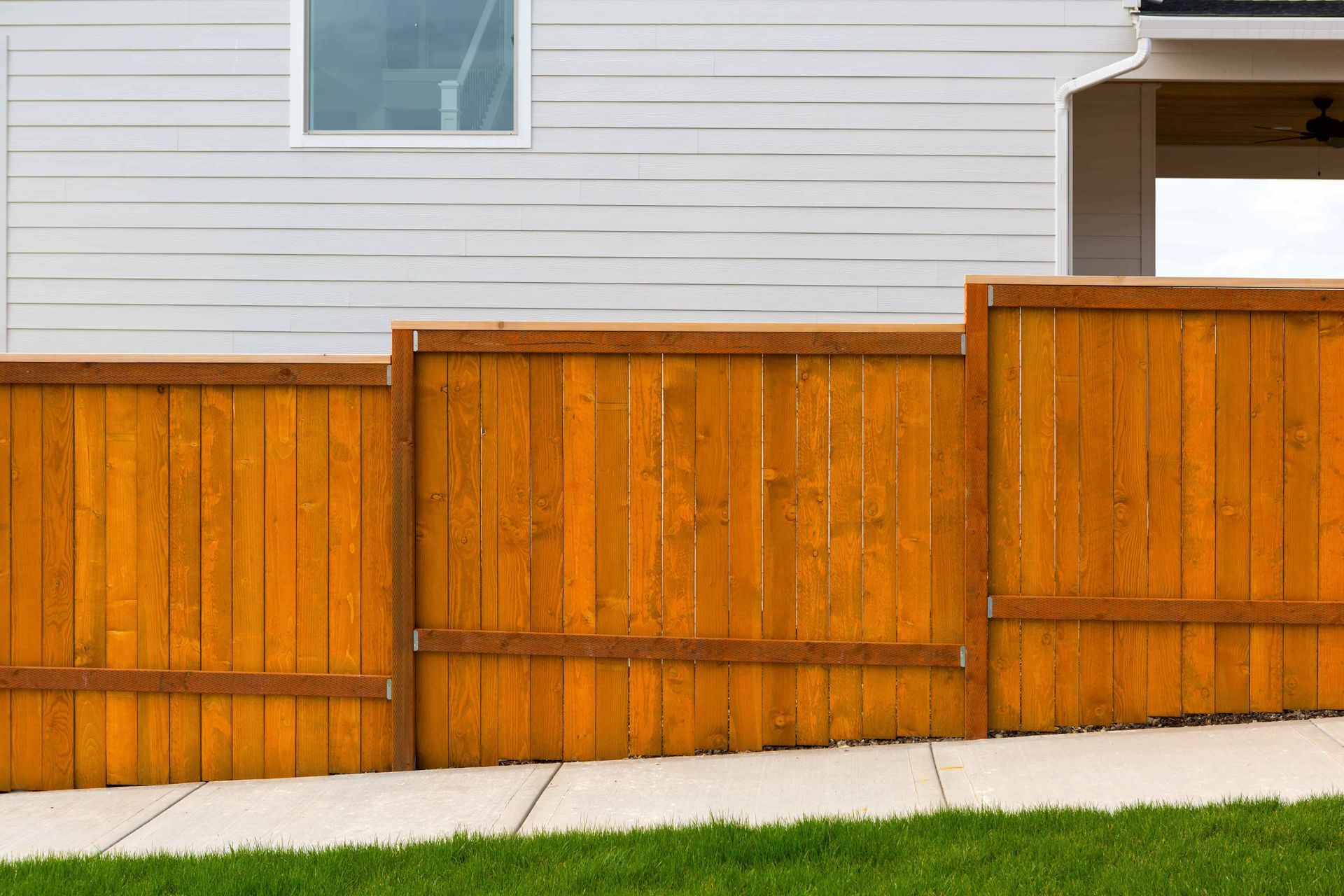 A wooden fence is sitting next to a sidewalk in front of a house.