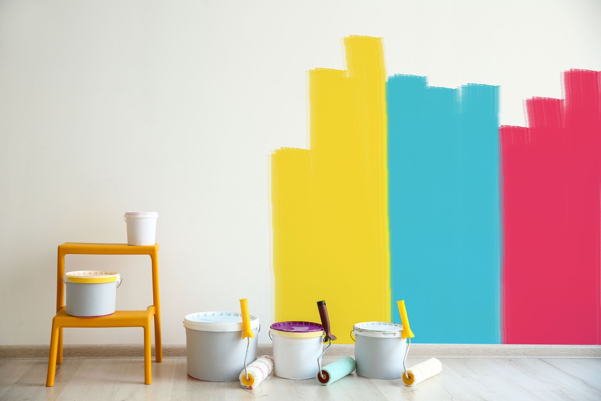 A wall is being painted in different colors with paint buckets and rollers.