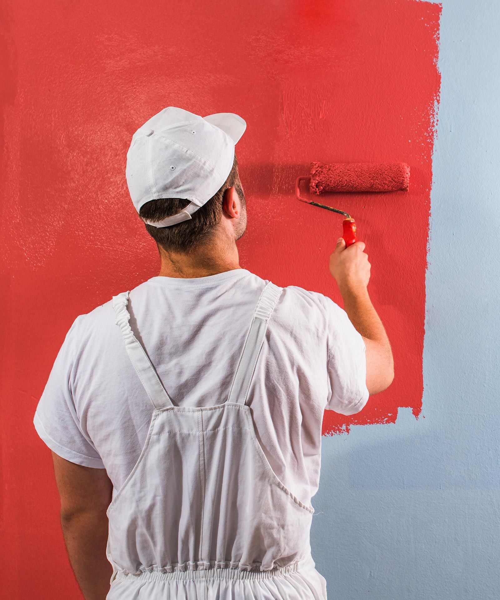 A man is painting a wall red with a roller.