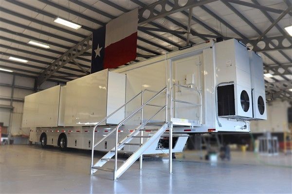 A large white trailer with stairs and a texas flag in the background