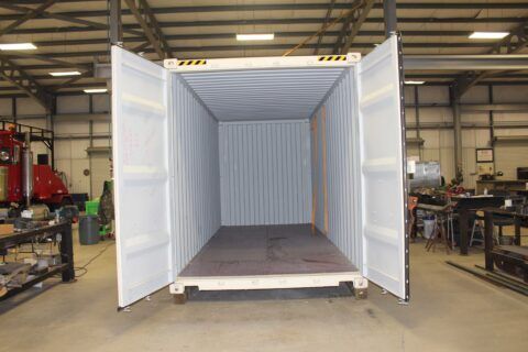 An empty shipping container is sitting in a warehouse with its doors open.