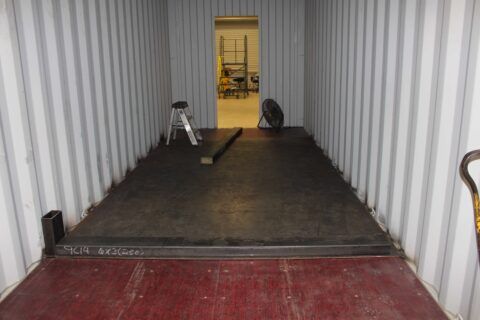 The inside of a shipping container with a red floor and a ladder.