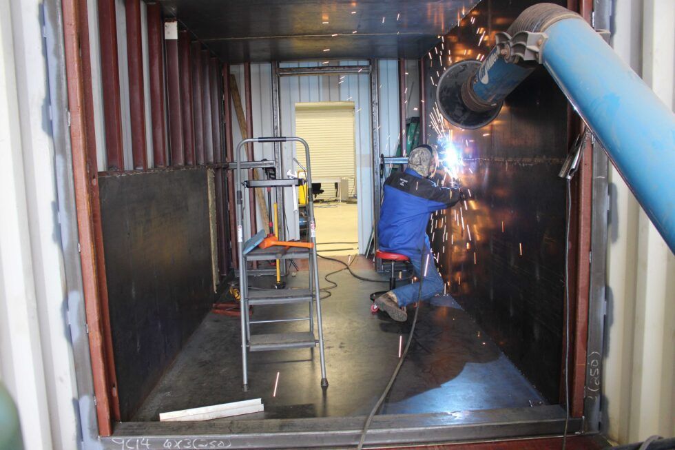 A man is welding inside of a shipping container