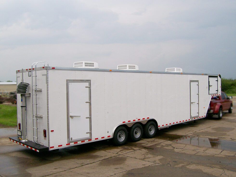 A white trailer is parked next to a red truck