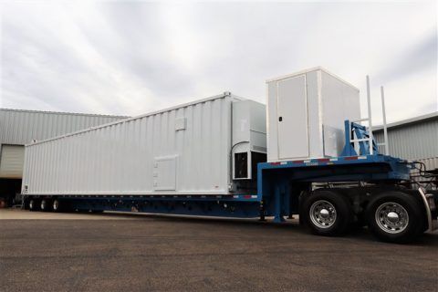 A large semi truck with a white trailer attached to it is parked in front of a building.