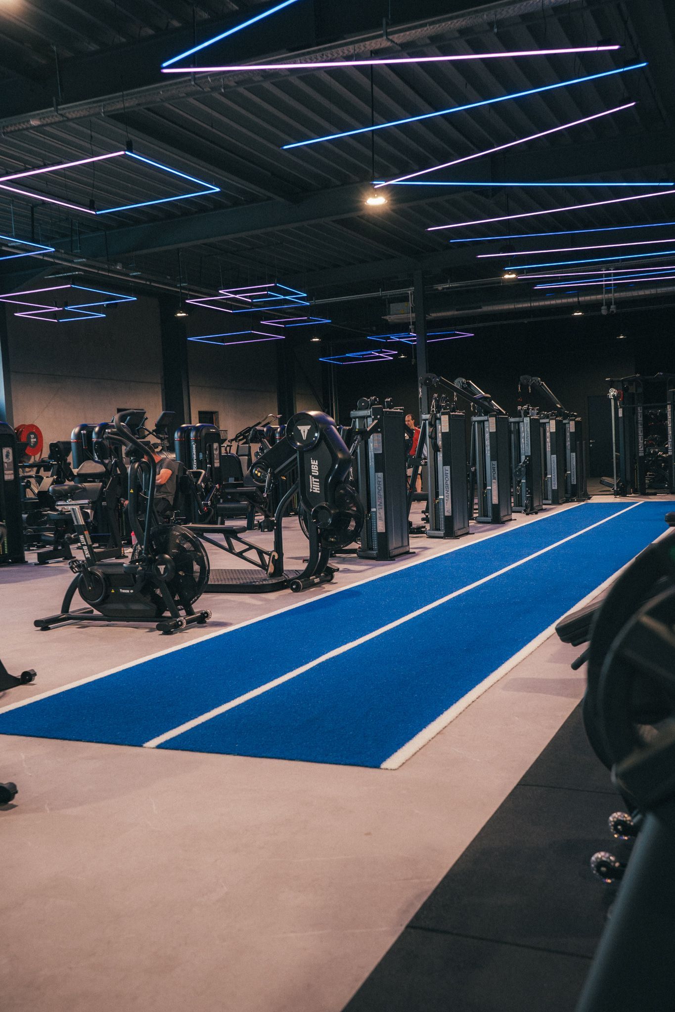 Sportschoolinterieur met blauwe baan en fitnessapparaten. Verlicht met neonverlichting.