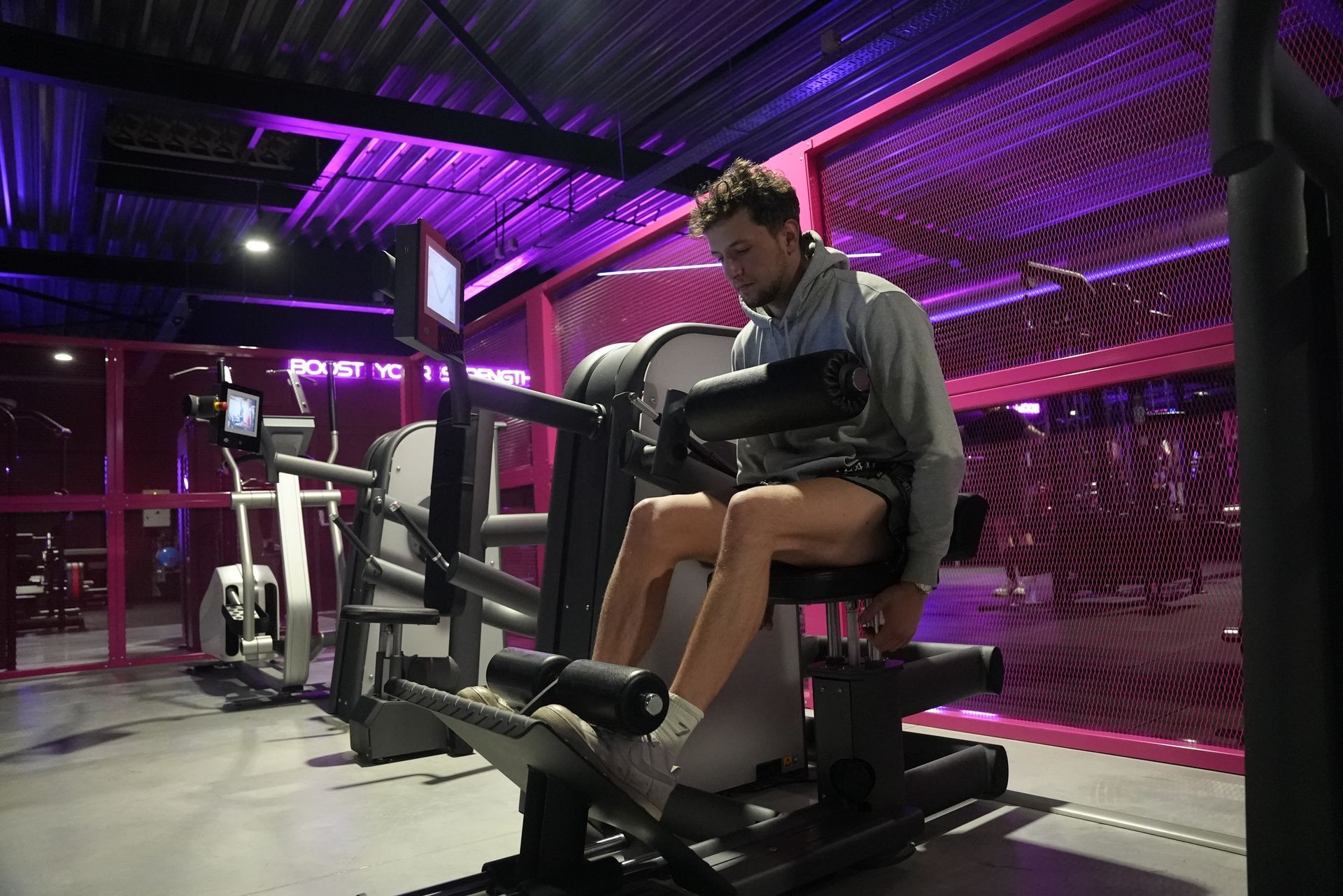 Man gebruikt een leg press-apparaat in een sportschool met paarse en zwarte accenten.
