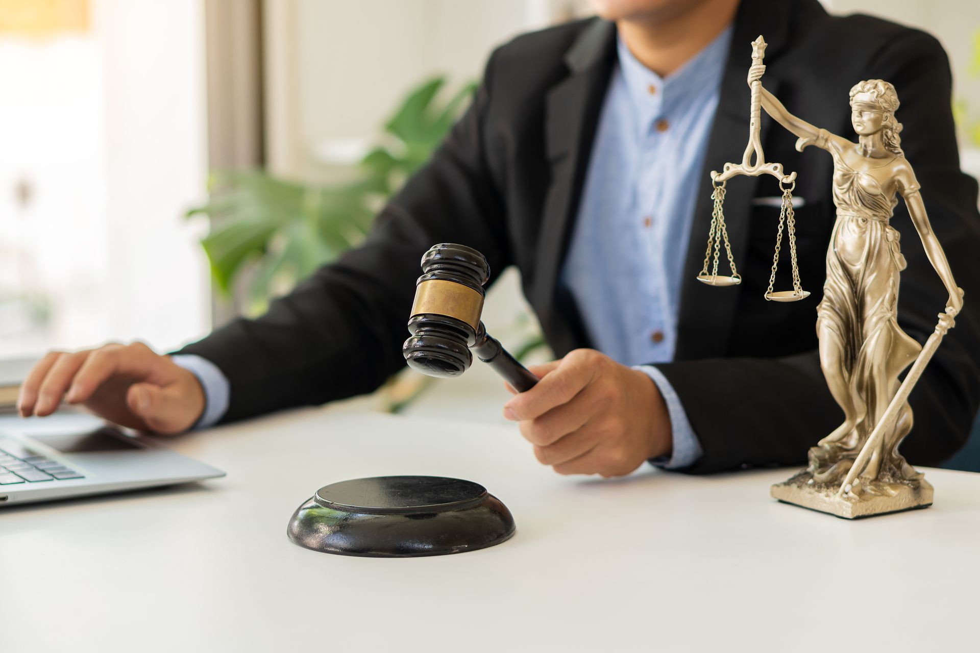 A man is holding a gavel in front of a statue of justice.