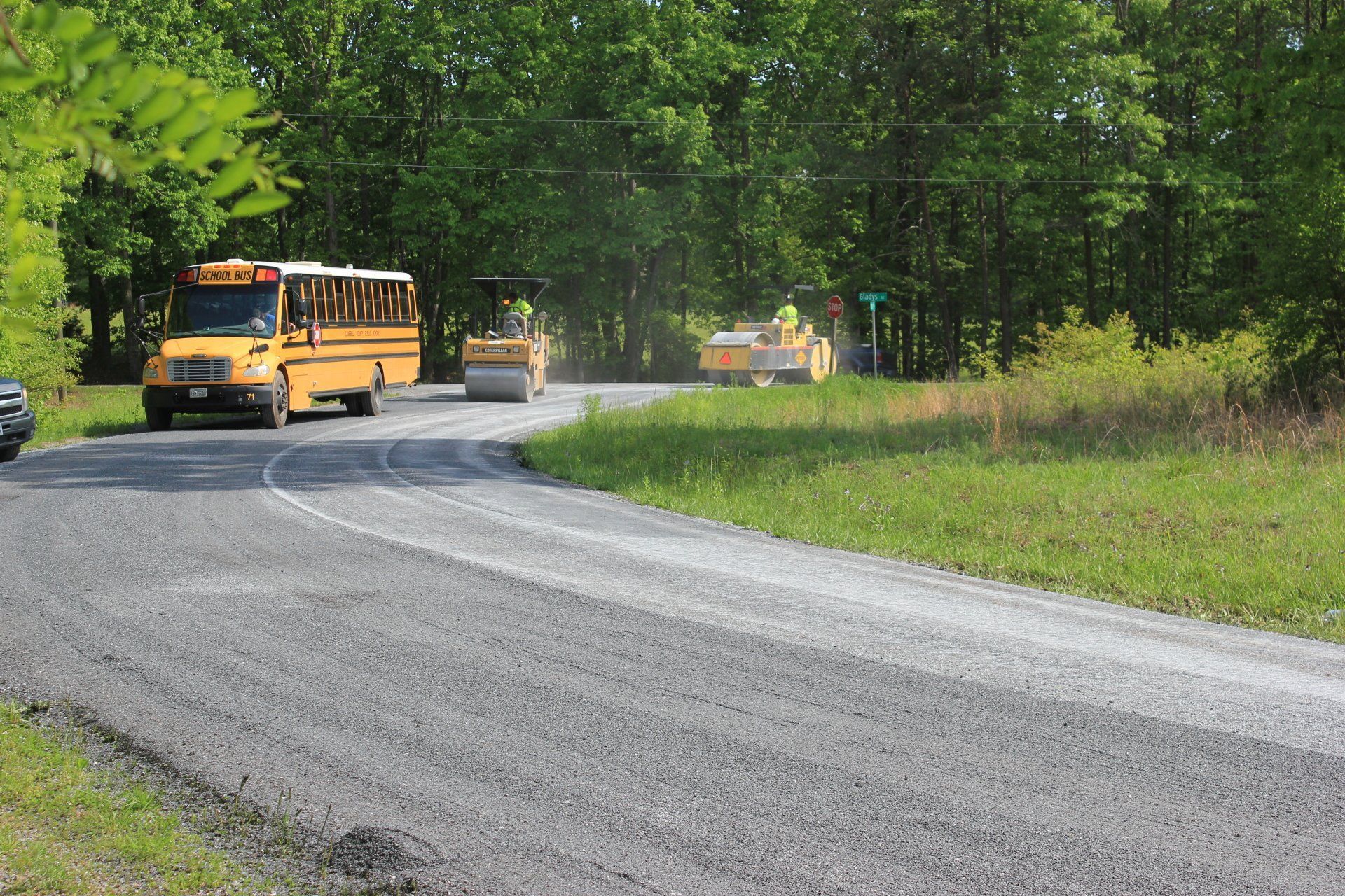 Chip seal surface being rolled with school bus nearby.