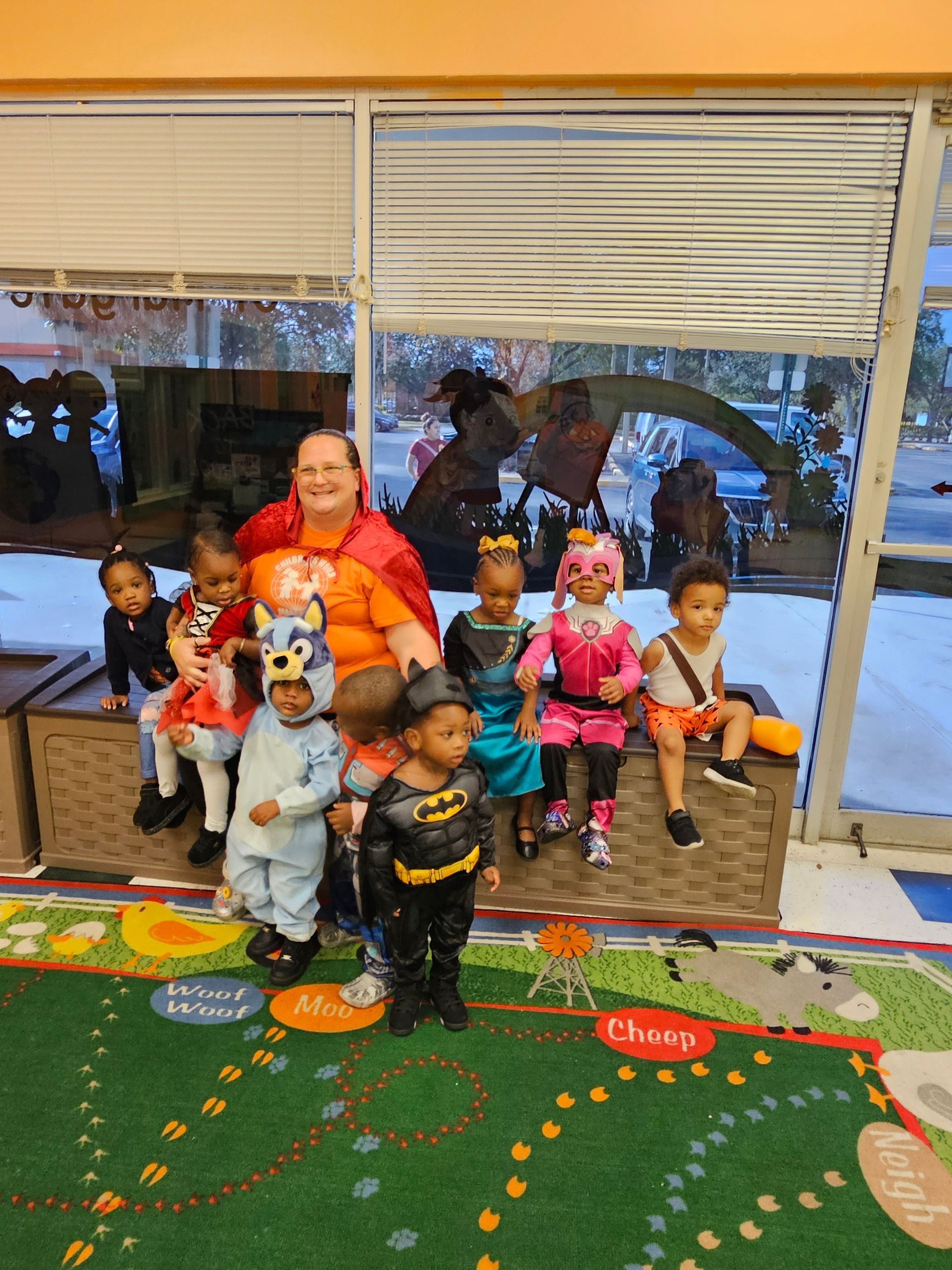 A group of children and an adult dressed in costumes, posing inside near a window.