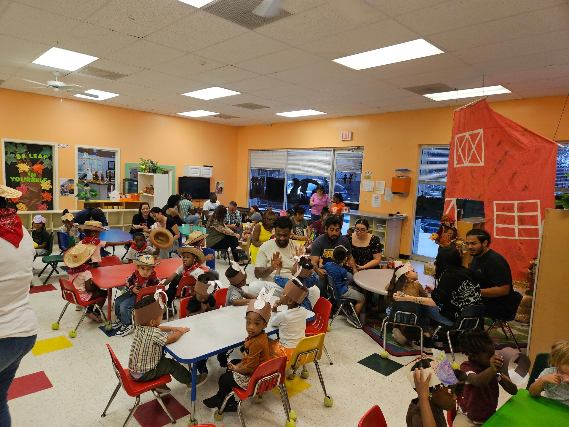 Children line up in a playground, some holding toys, under the supervision of adults.