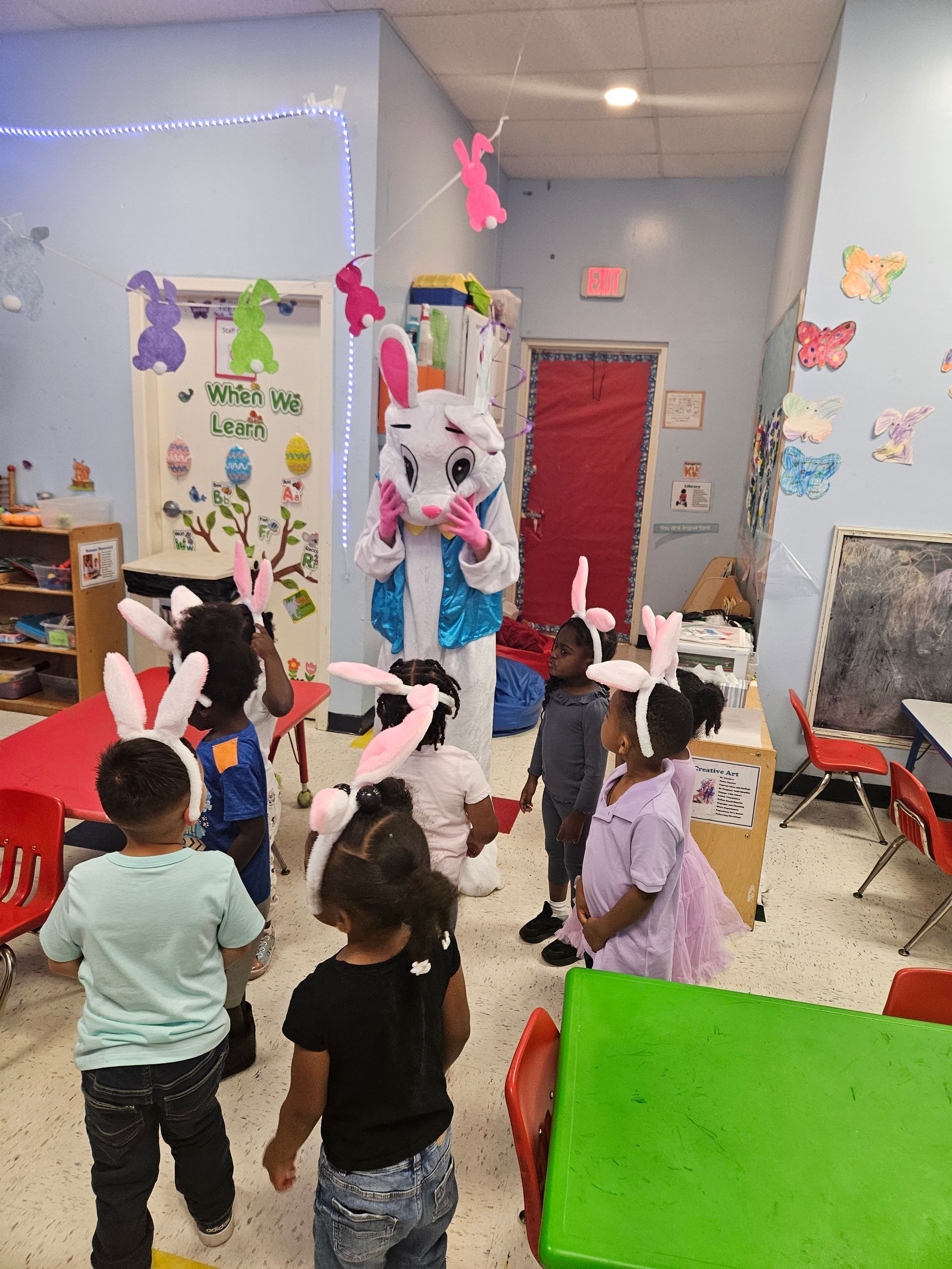 A group of children sitting on a colorful rug in a classroom, holding teddy bears.