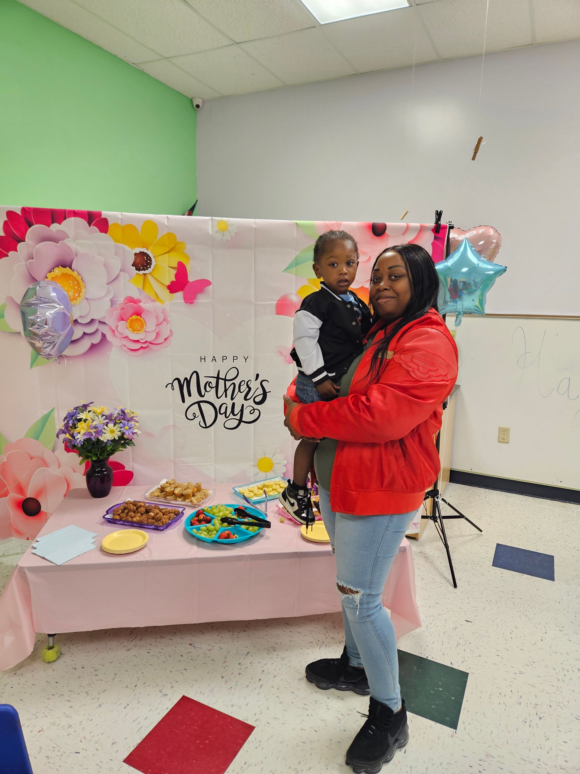 Woman in red jacket holds a child in front of a 