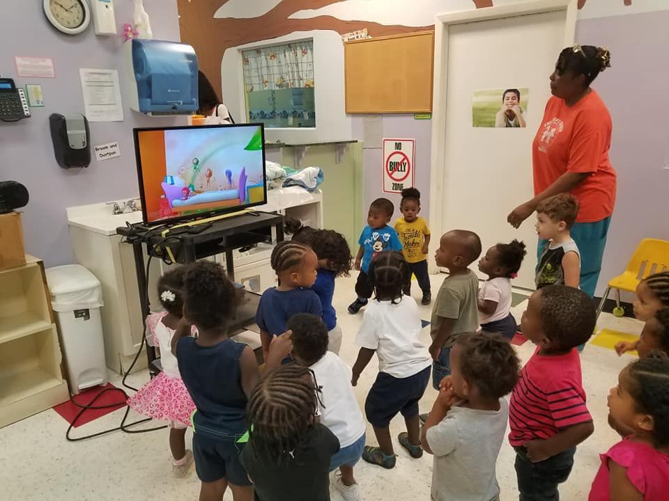 Children watch TV with a teacher in a preschool classroom.