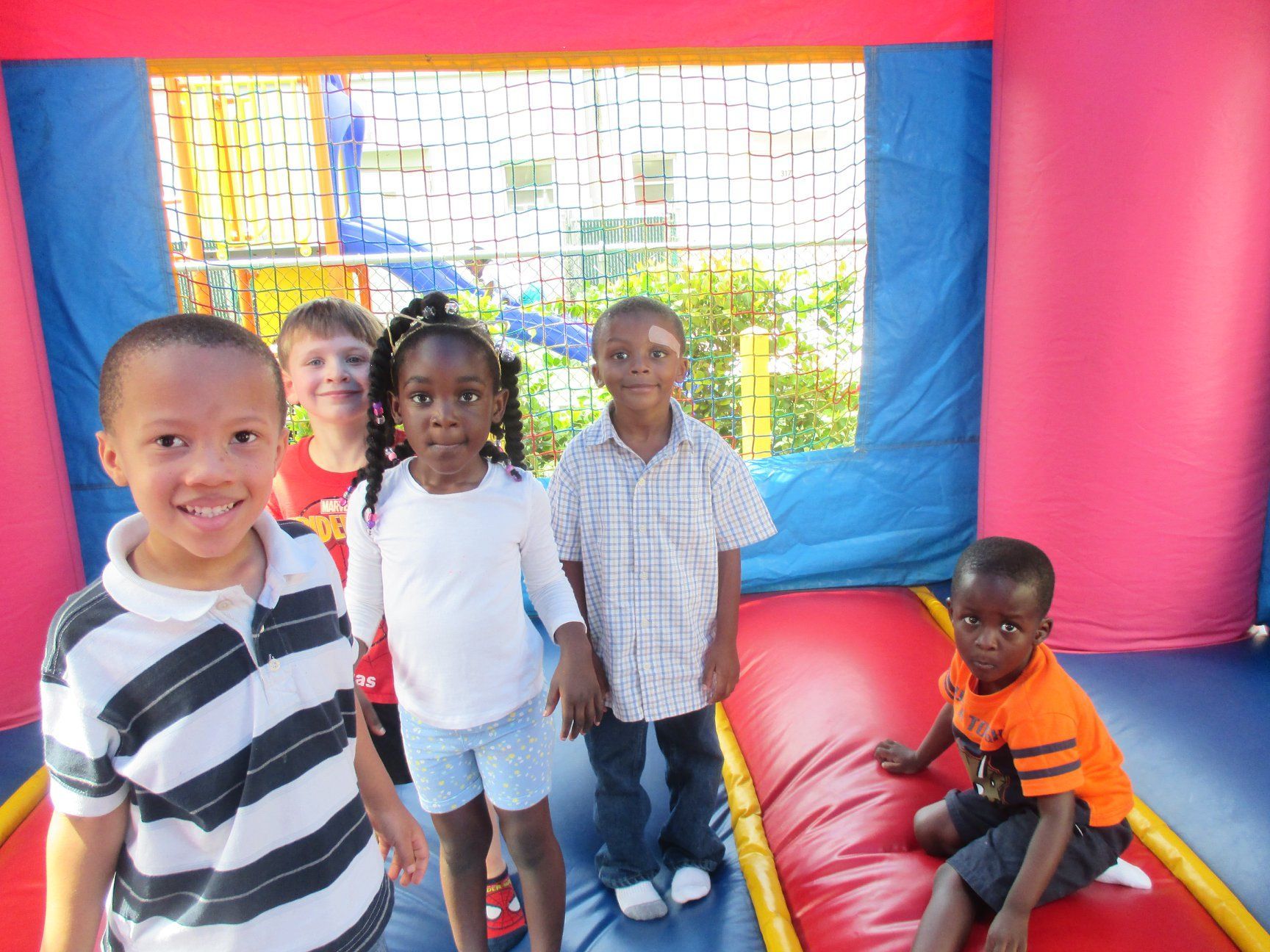 Children inside a bouncy castle, smiling. A few are standing, one is sitting, with colorful walls.