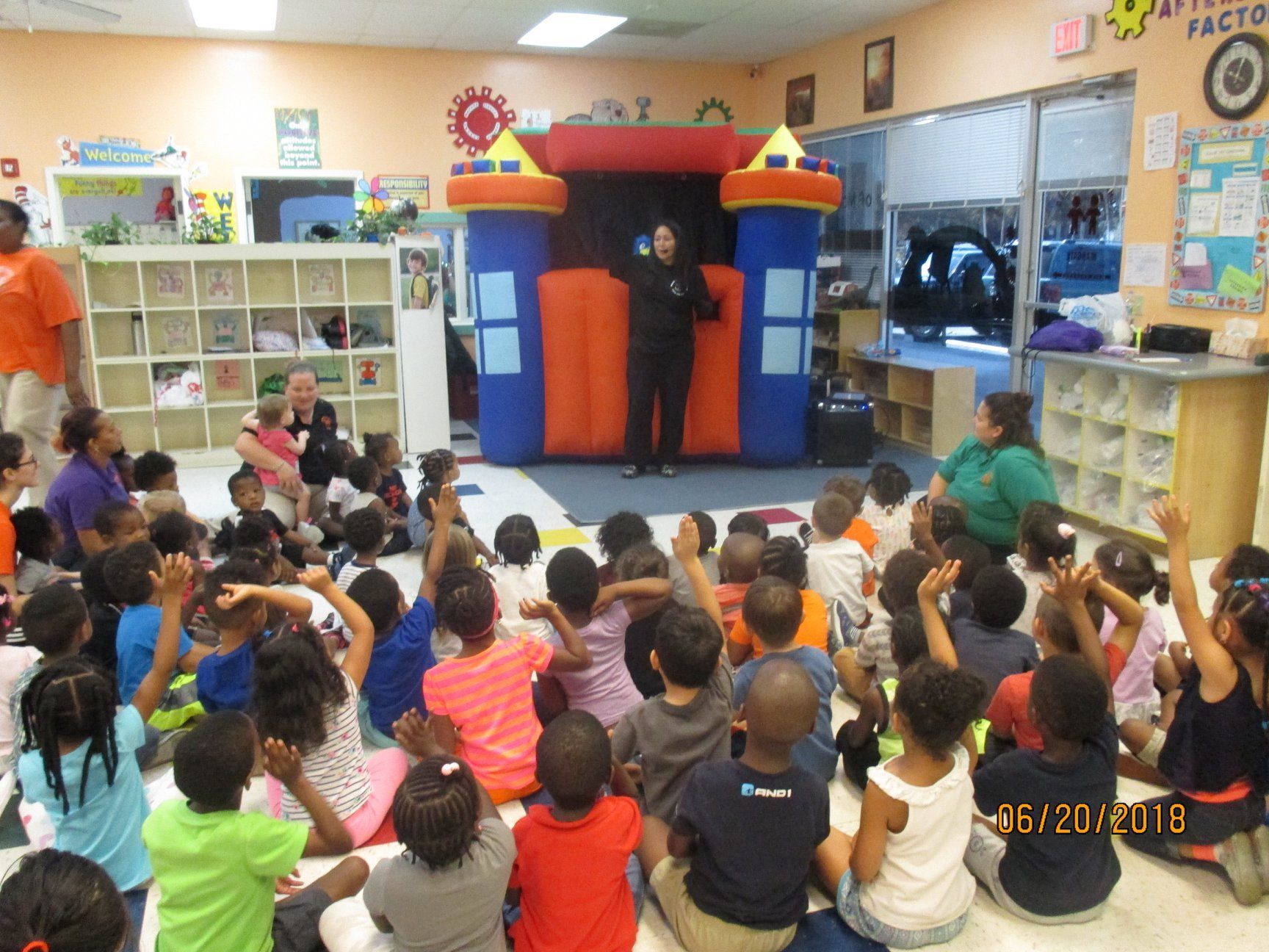 Children sitting on floor in a classroom, raising their hands during a presentation with a castle-shaped inflatable.