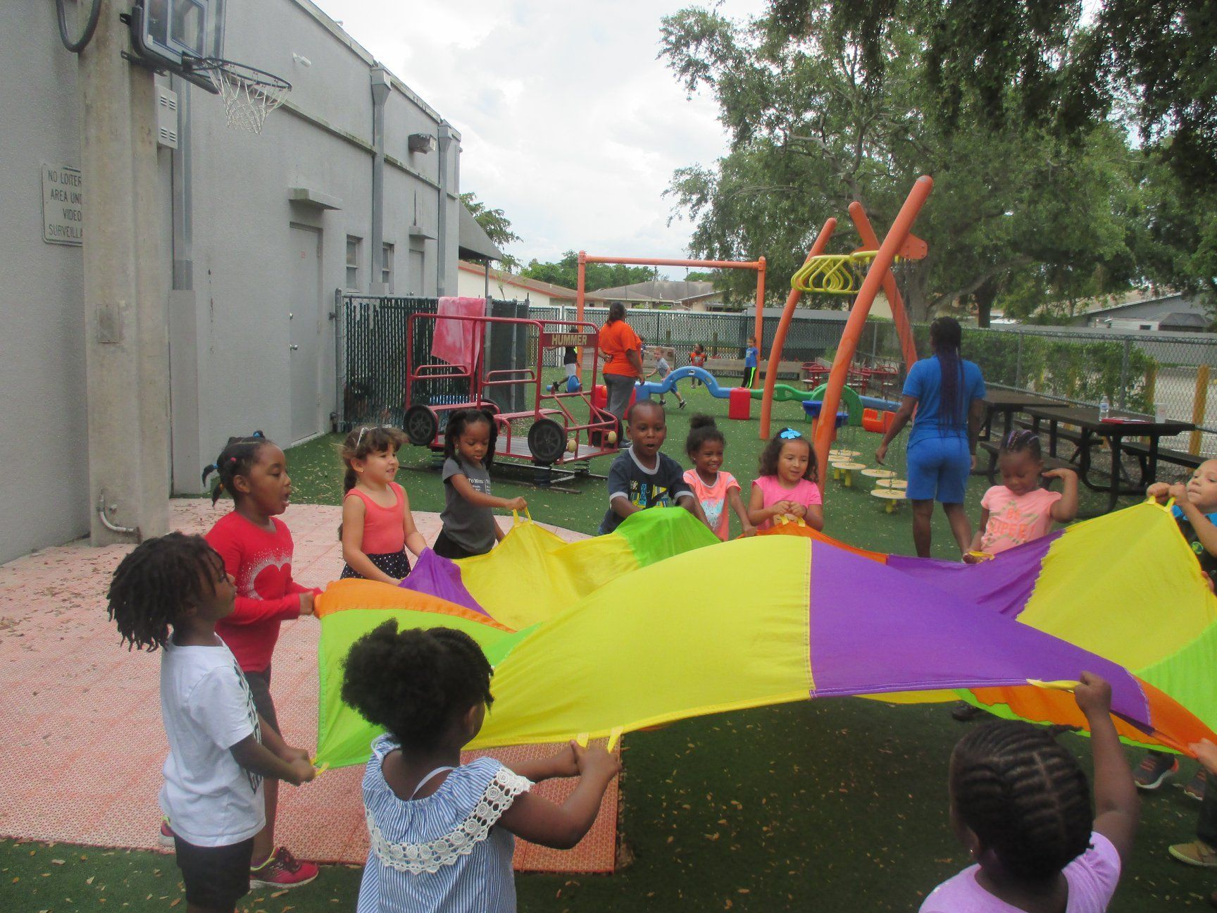 Children playing with a colorful parachute on a playground, sunny day.