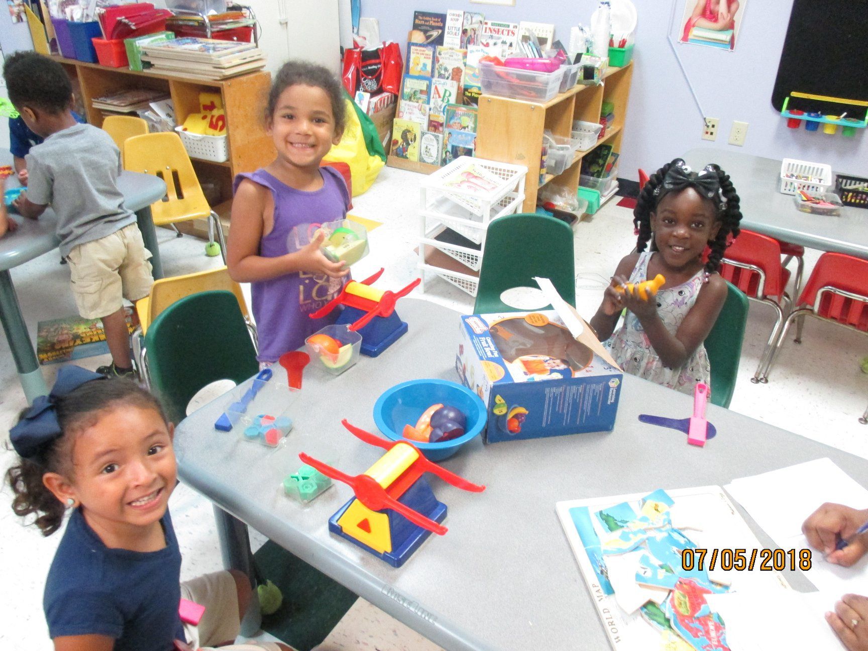 Children playing with toys and art supplies at a table in a classroom.