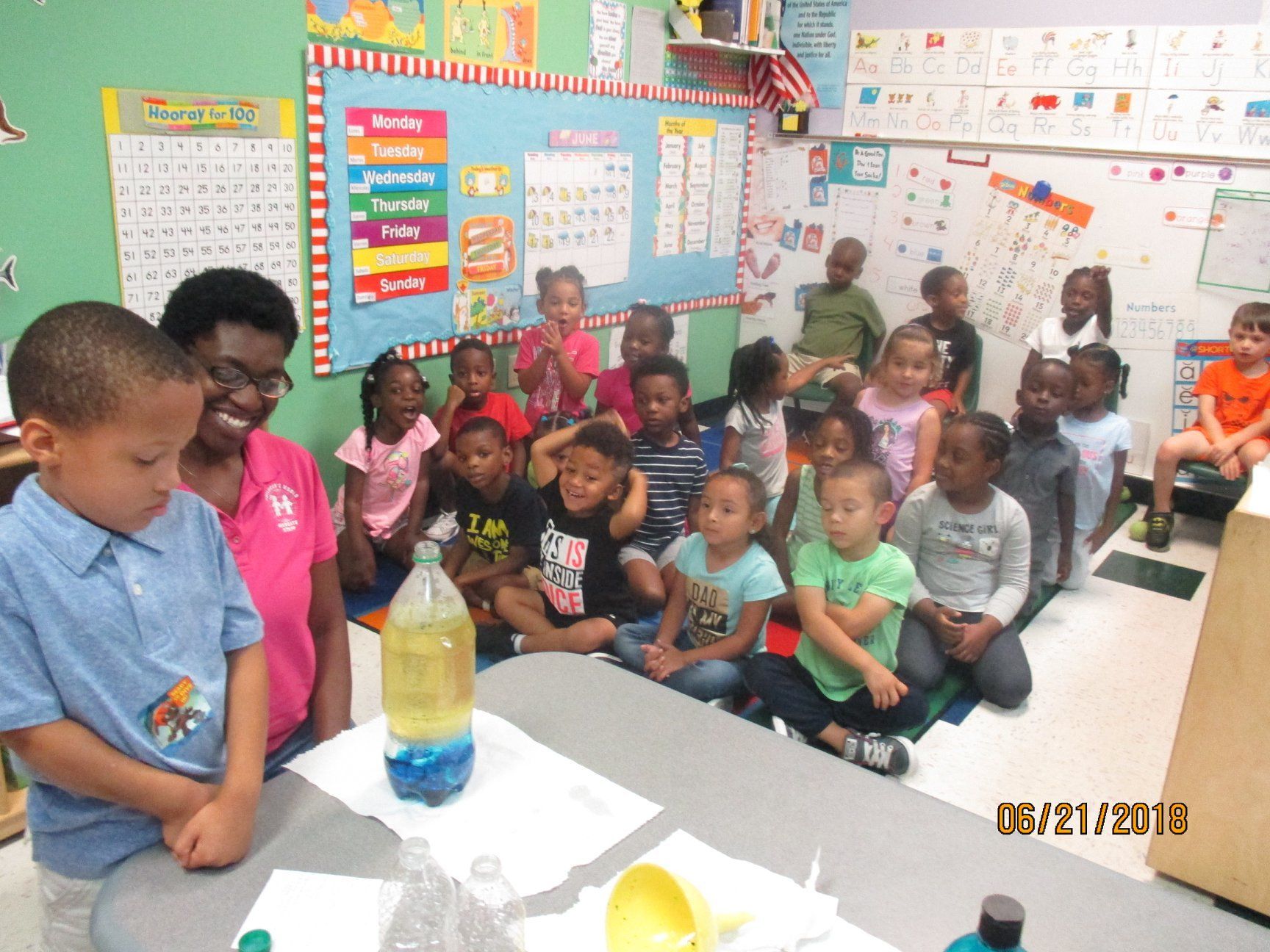 Children in a classroom watch a science experiment with a teacher.