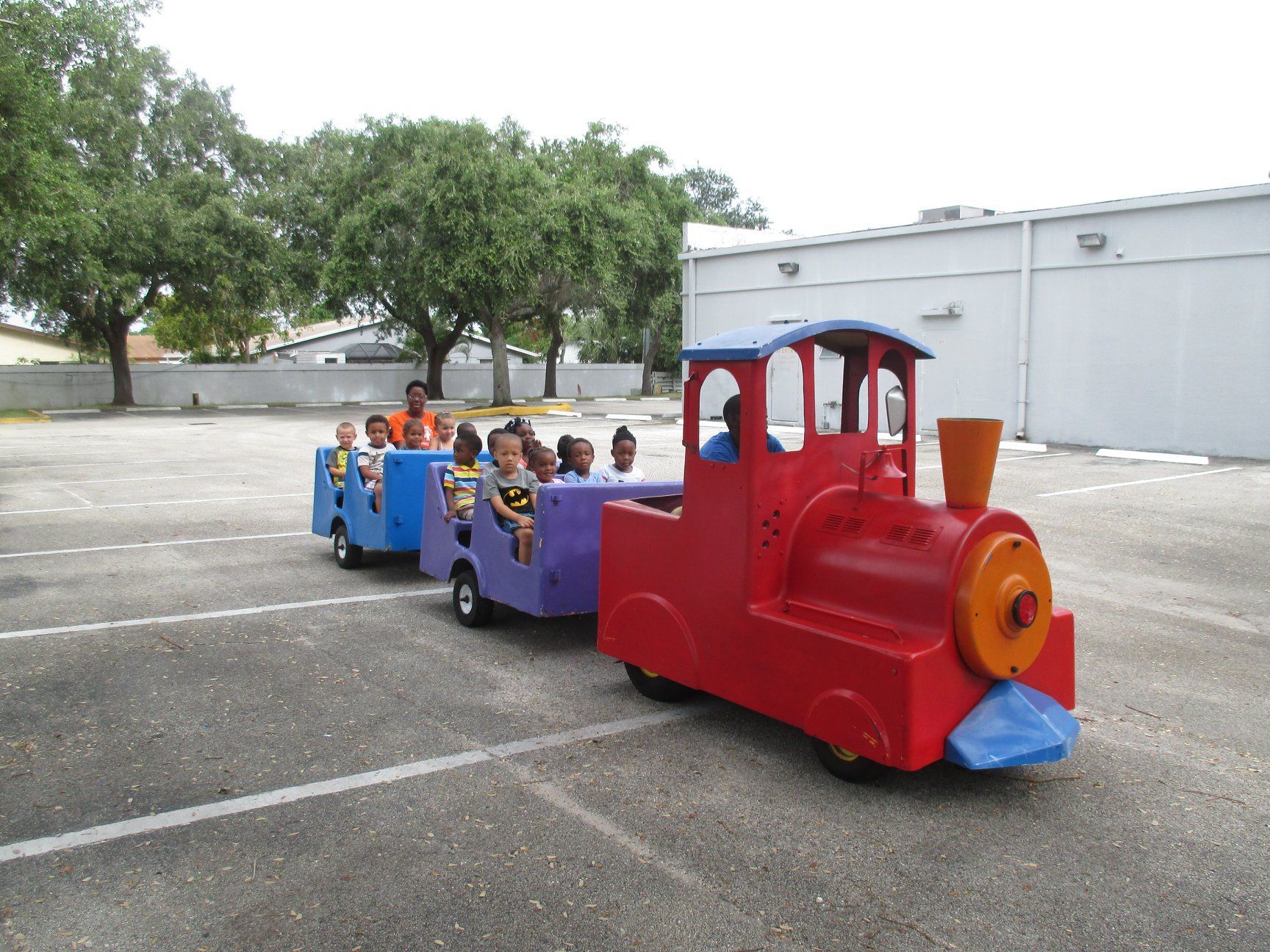 A colorful toy train carrying children in a parking lot.