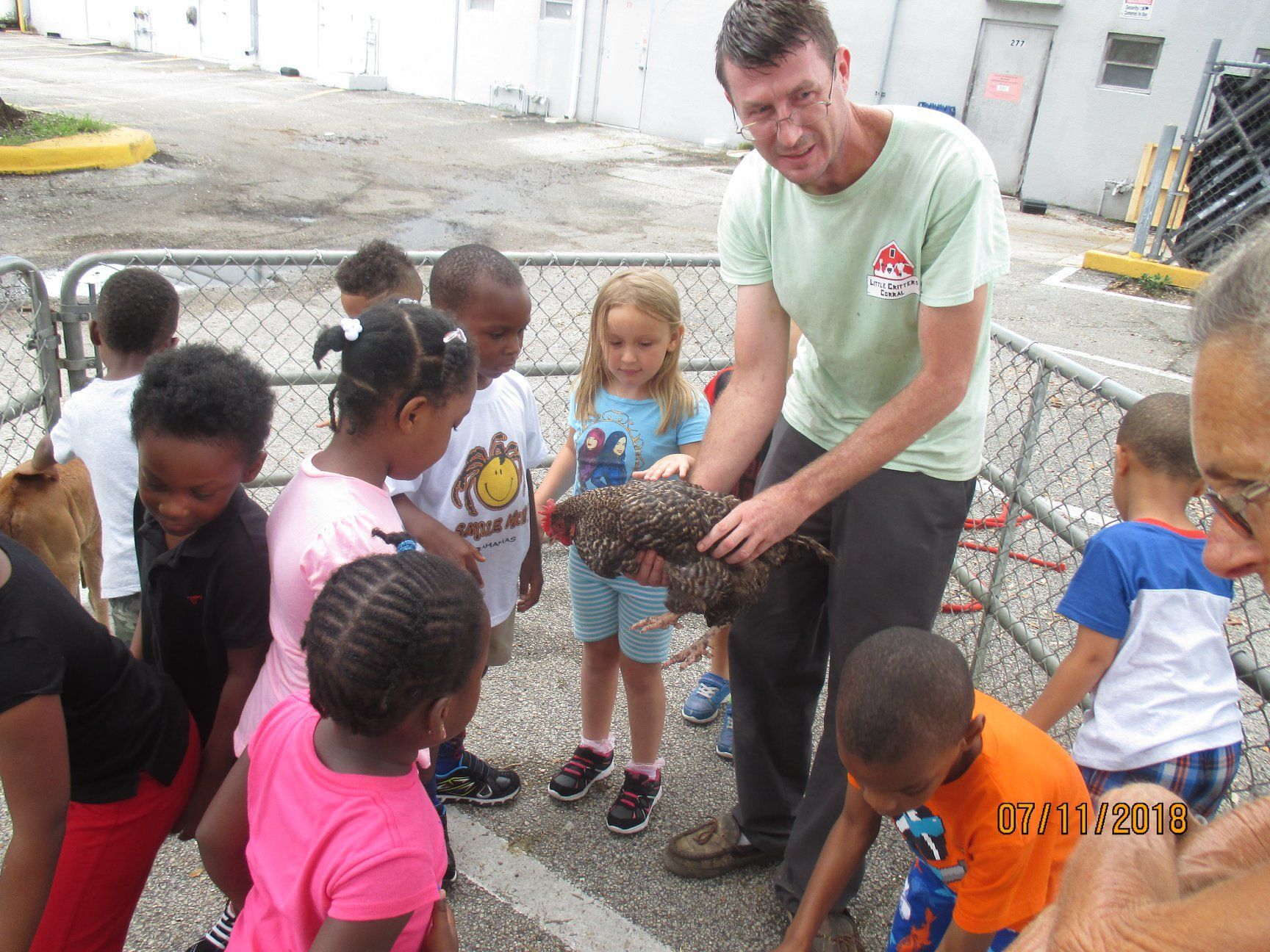 A man holds a bird, surrounded by children outside. They are looking at the bird in amazement.