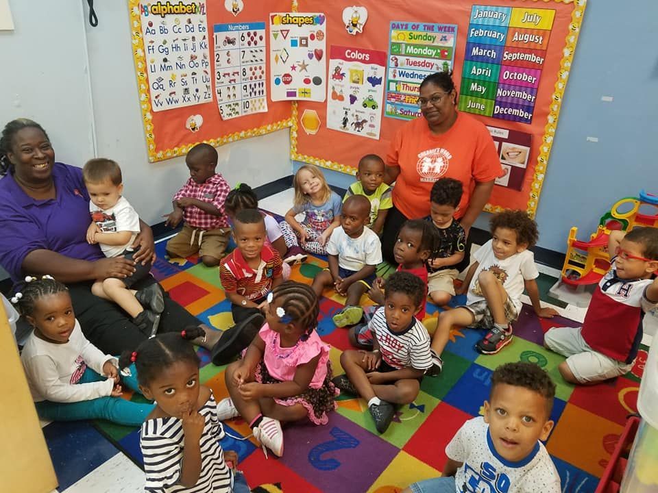 Children and two teachers seated on a colorful rug in a classroom.