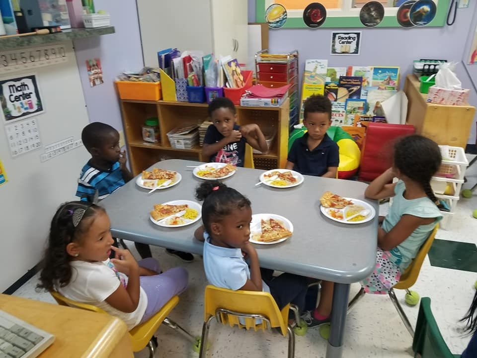 Children seated around a table, eating pizza in a classroom.