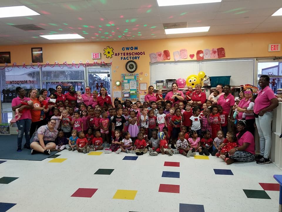 Group of children and adults in pink shirts at a school, smiling.