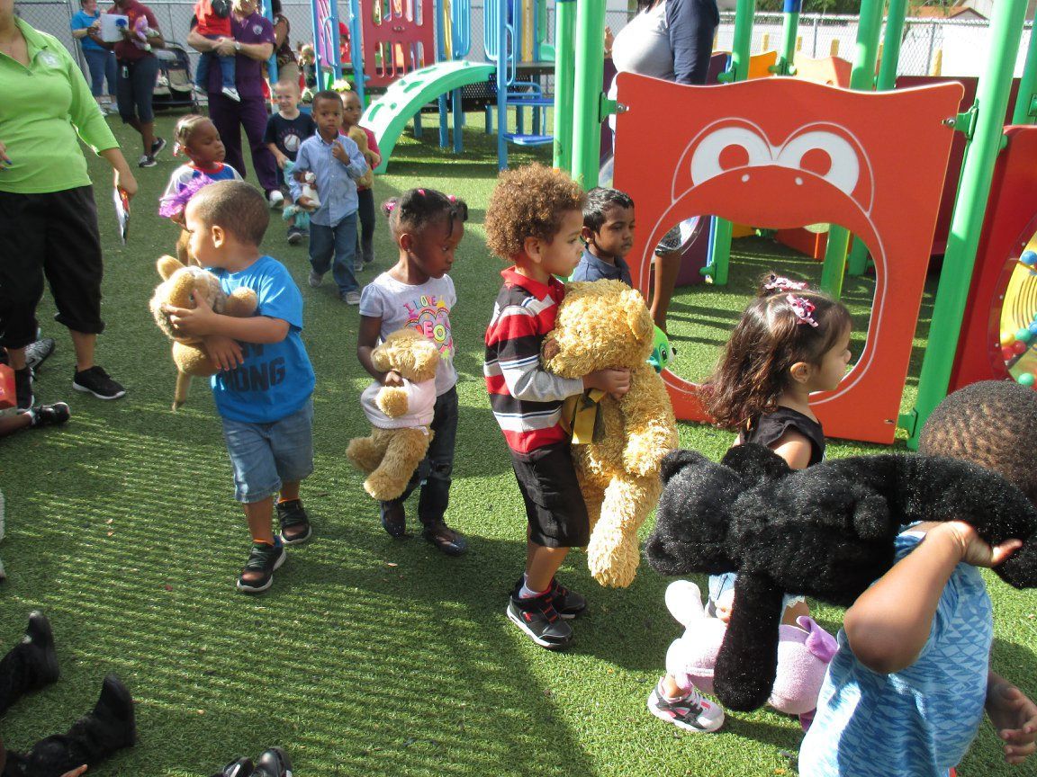 Children on a playground holding teddy bears, walking.