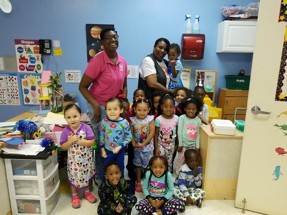 A group of children and two teachers smile in a bright classroom.