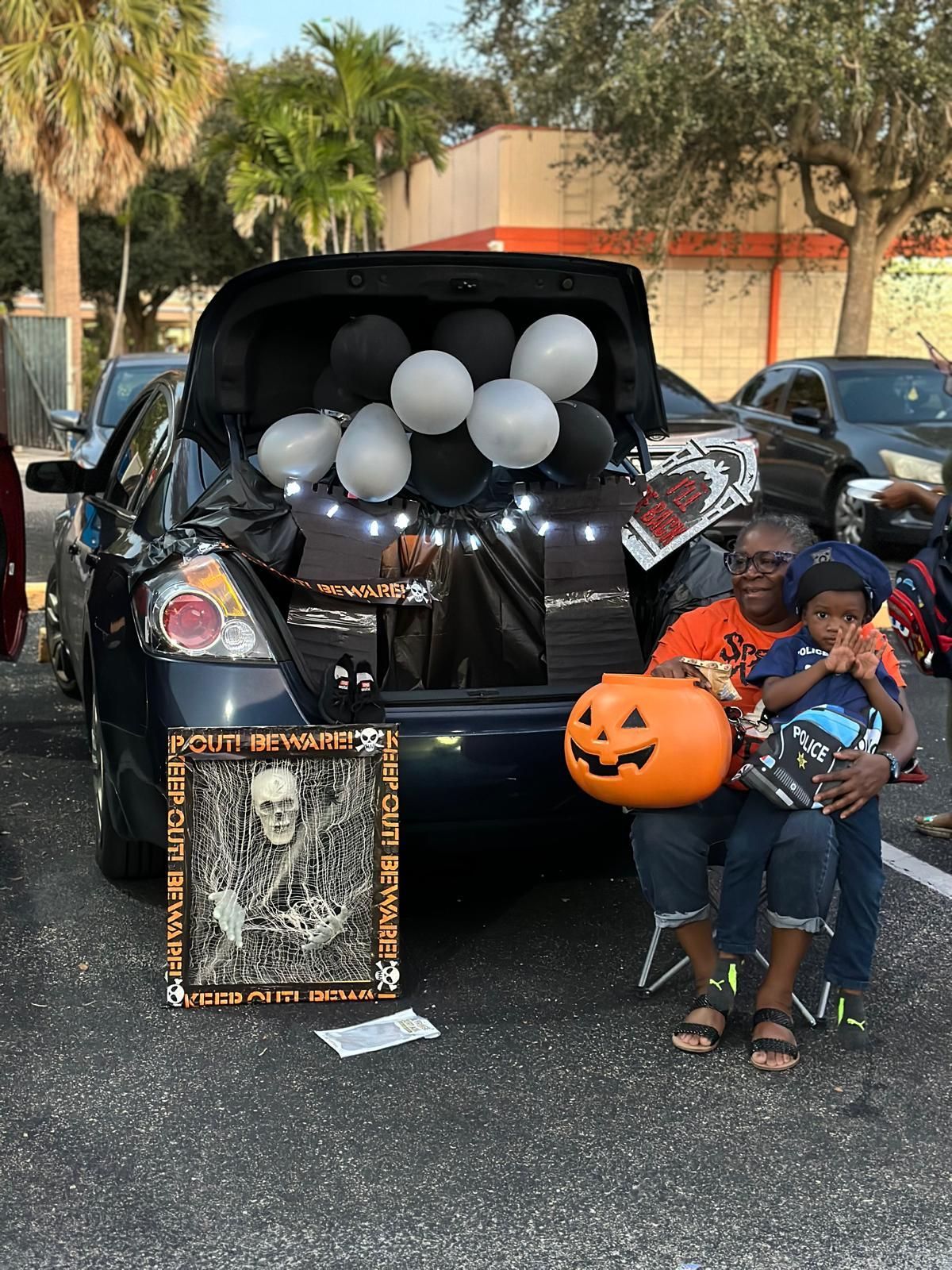 A woman and child pose for a photo in front of a Halloween-decorated car trunk.