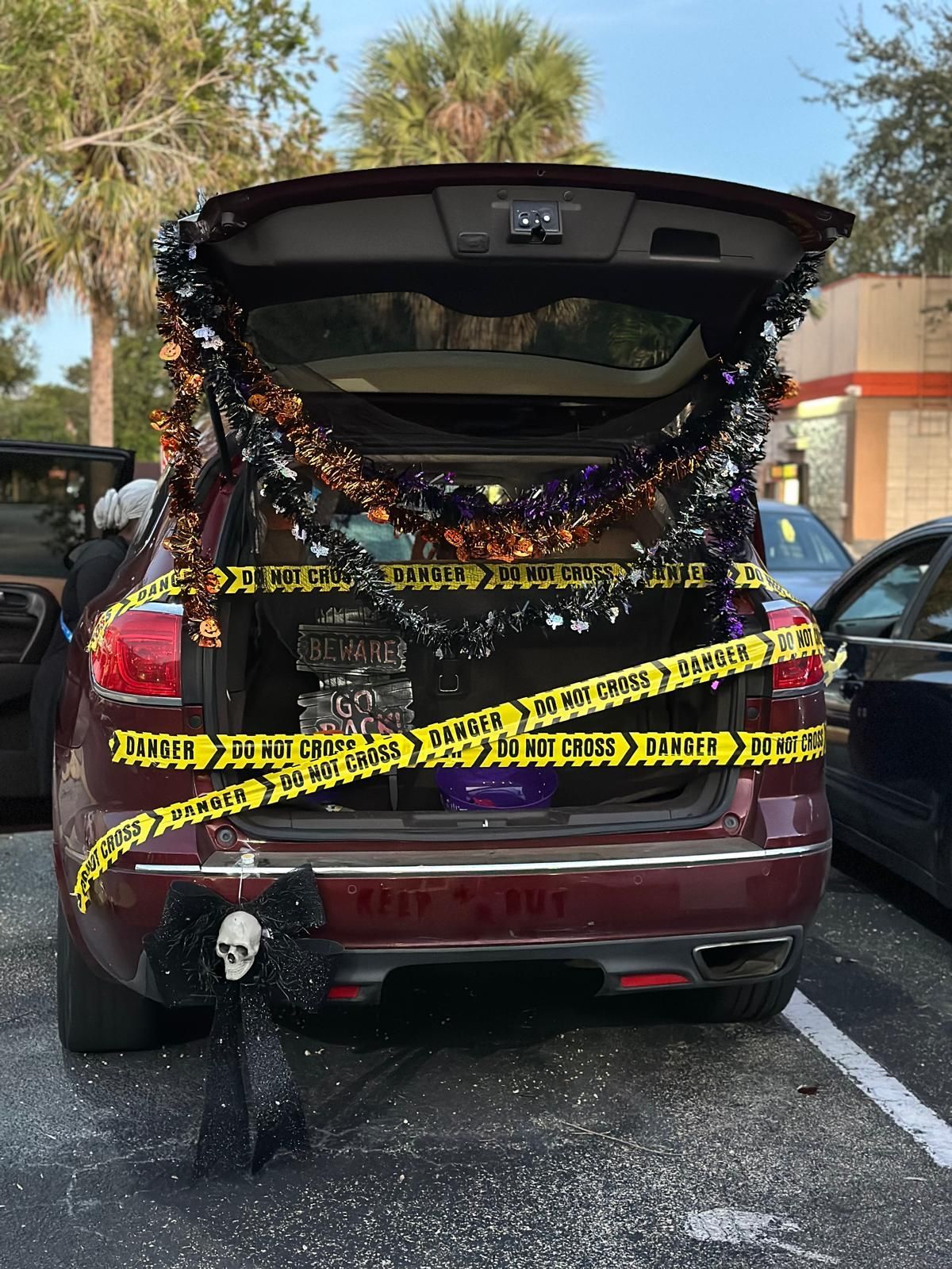 Red SUV decorated with Halloween garland and caution tape at a trunk-or-treat event.