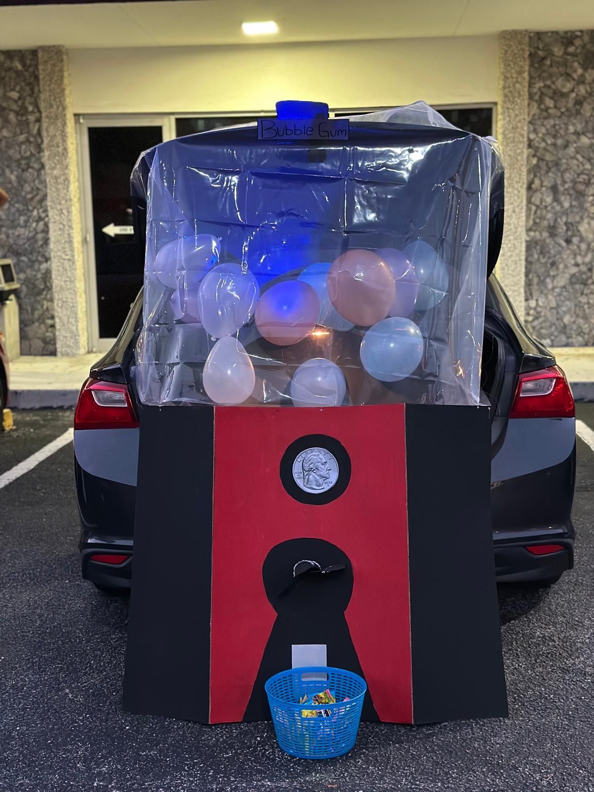 Car trunk decorated as a red and black machine with balloons inside and a basket for candy.