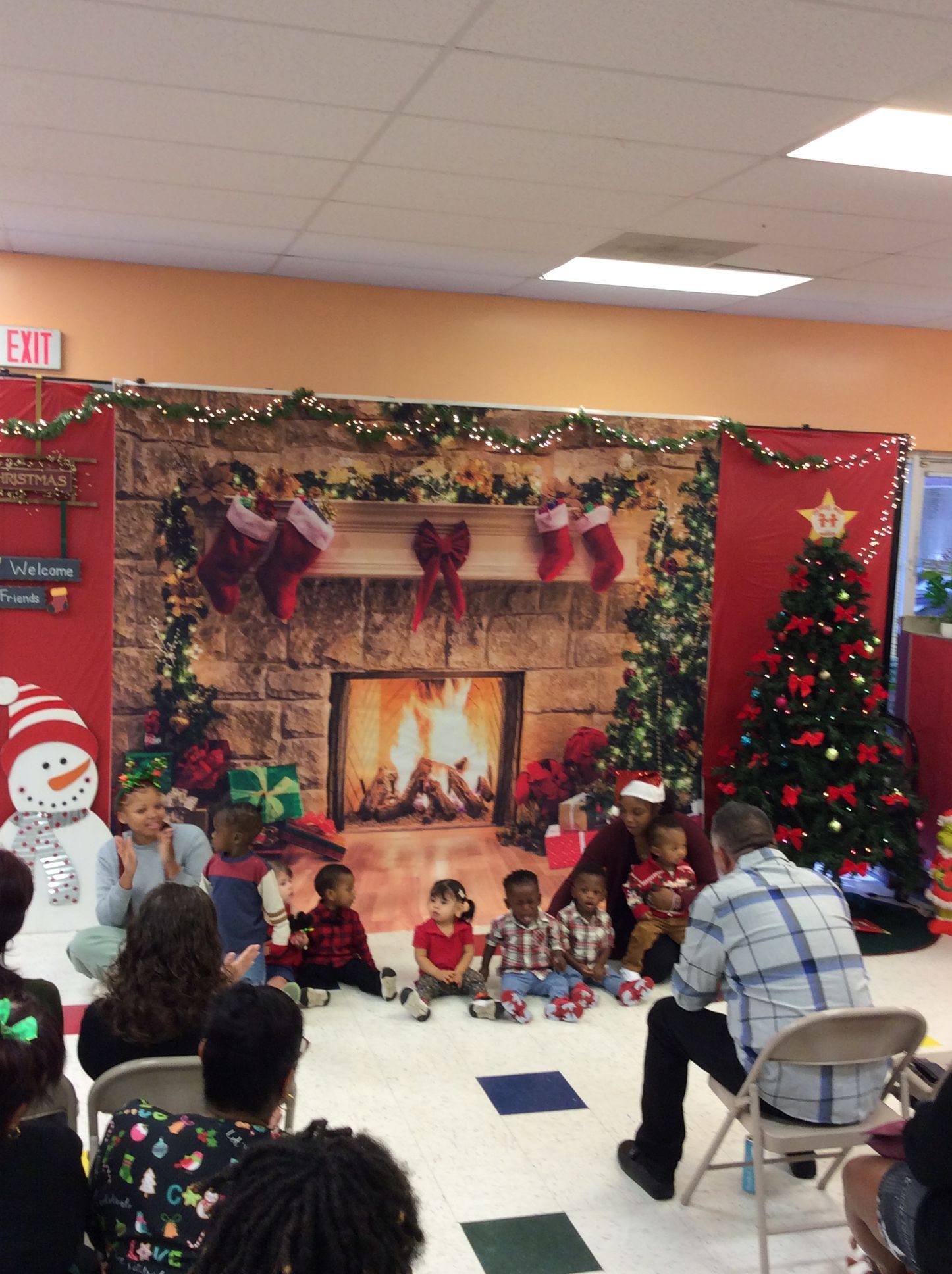 Children performing in front of a Christmas backdrop; a tree, a fireplace, and decorations.