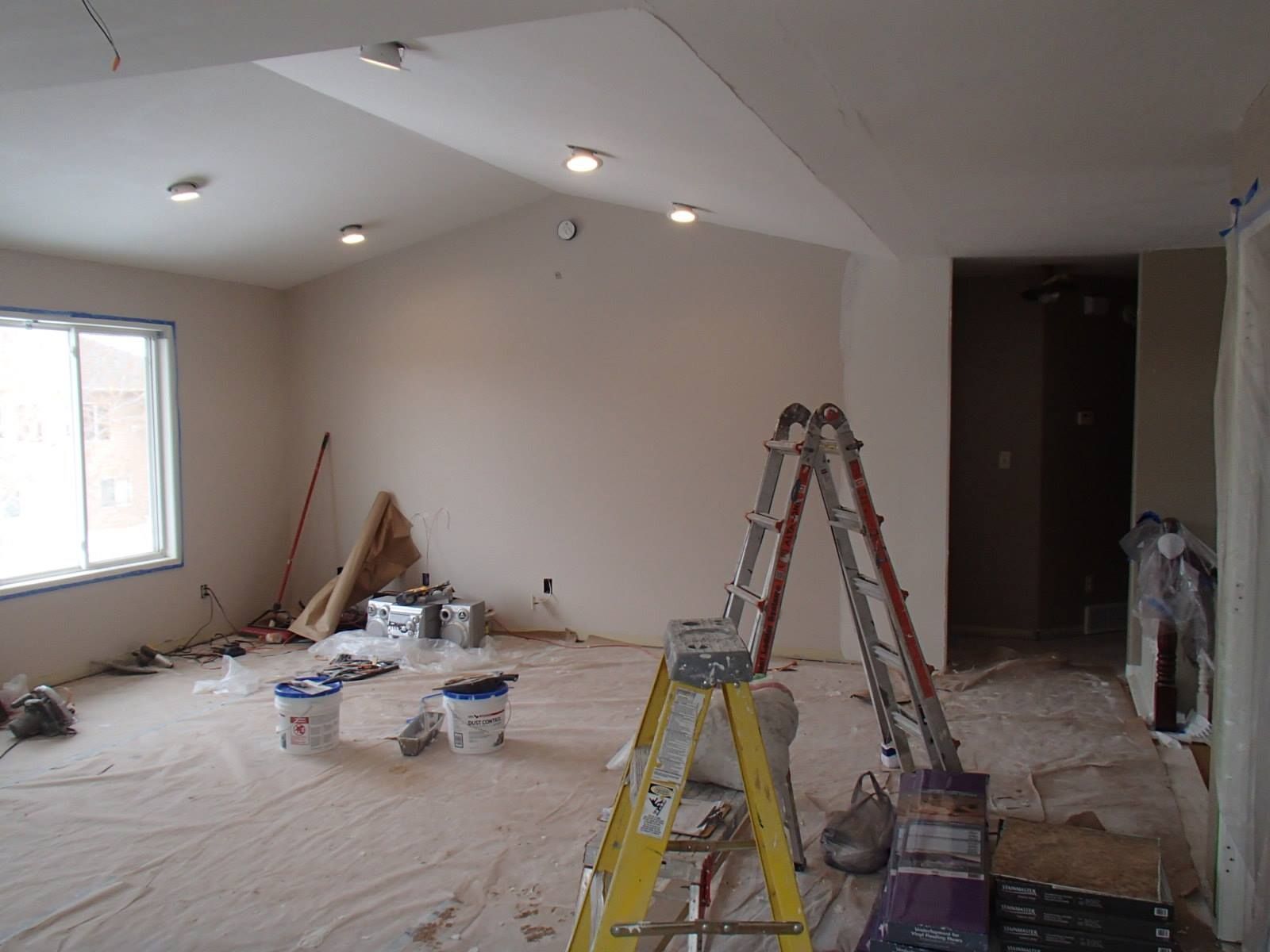Partially renovated room with ladders, tools, and covered floor under a sloped ceiling