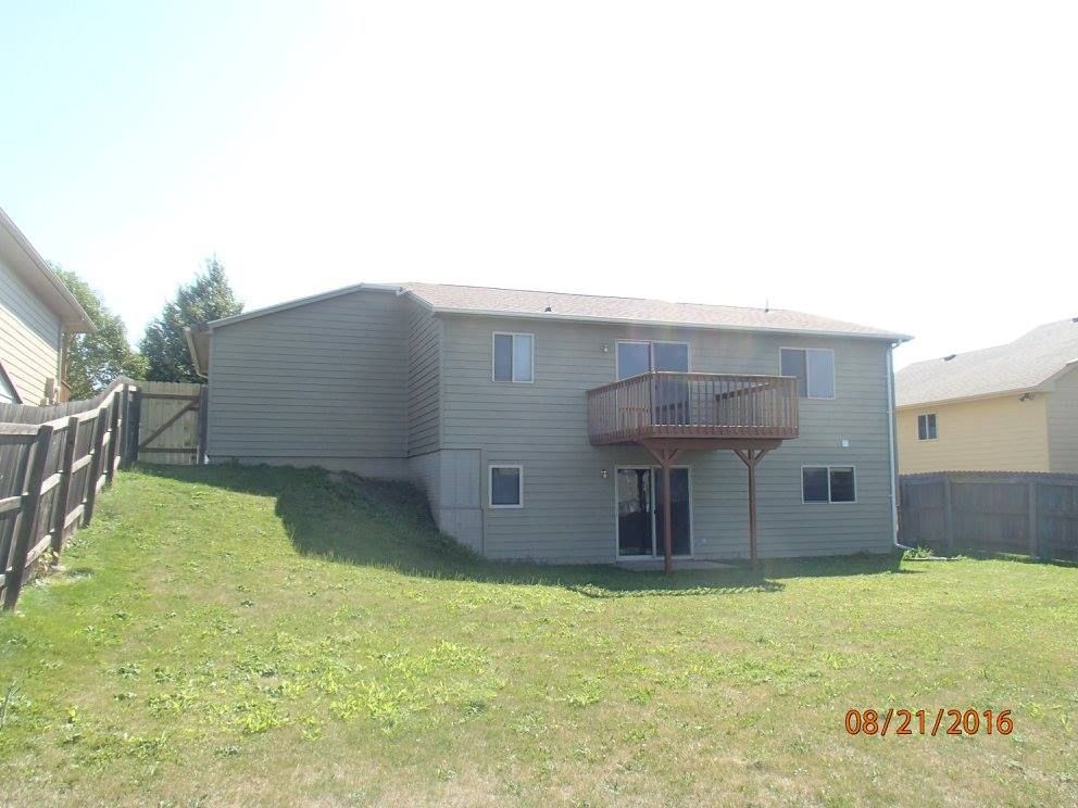 Back of a two-story house with a deck, on a grassy lawn, bordered by fences.