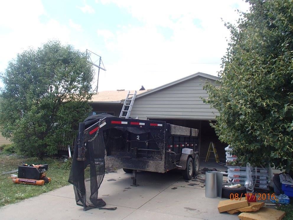 A trailer is parked in front of a house with a ladder on the roof.