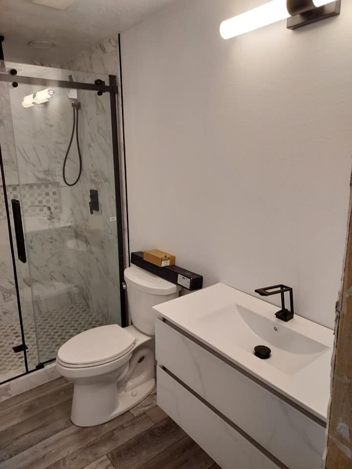 Modern white bathroom with glass shower, floating vanity, and black fixtures.