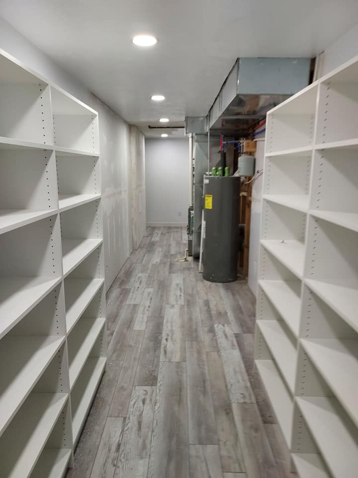 Long, narrow room with white shelving on either side, gray flooring, and a water heater at the end.