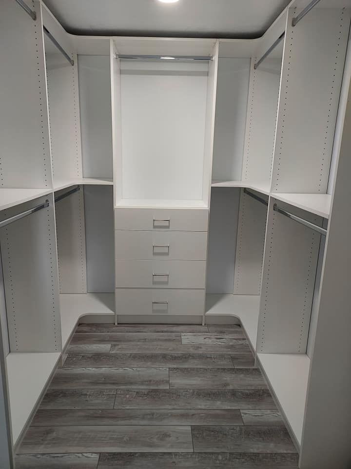 White walk-in closet with gray wood-look floor, shelves, drawers, and clothing rods.
