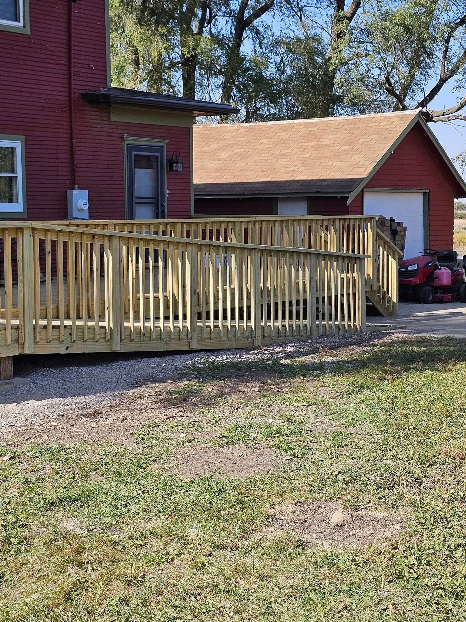 A wooden ramp leads to a red building's entrance. A garage and lawn are also visible.