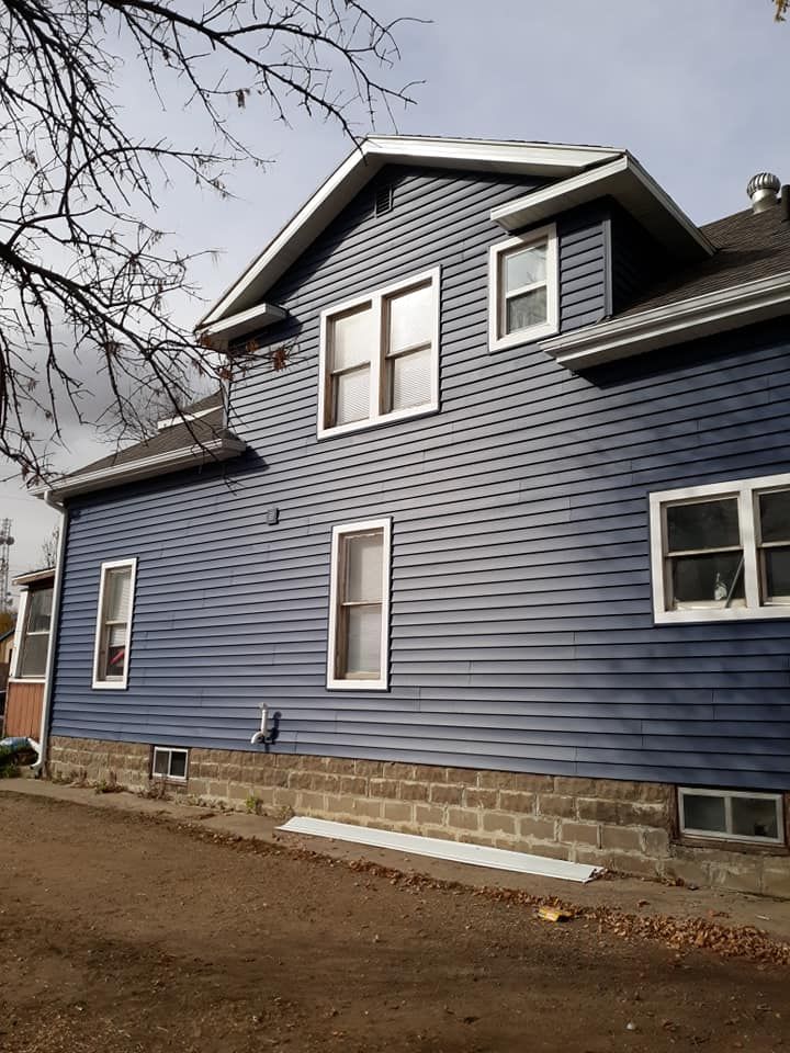 Blue-sided house with white window frames and a gray roof, set against a cloudy sky.