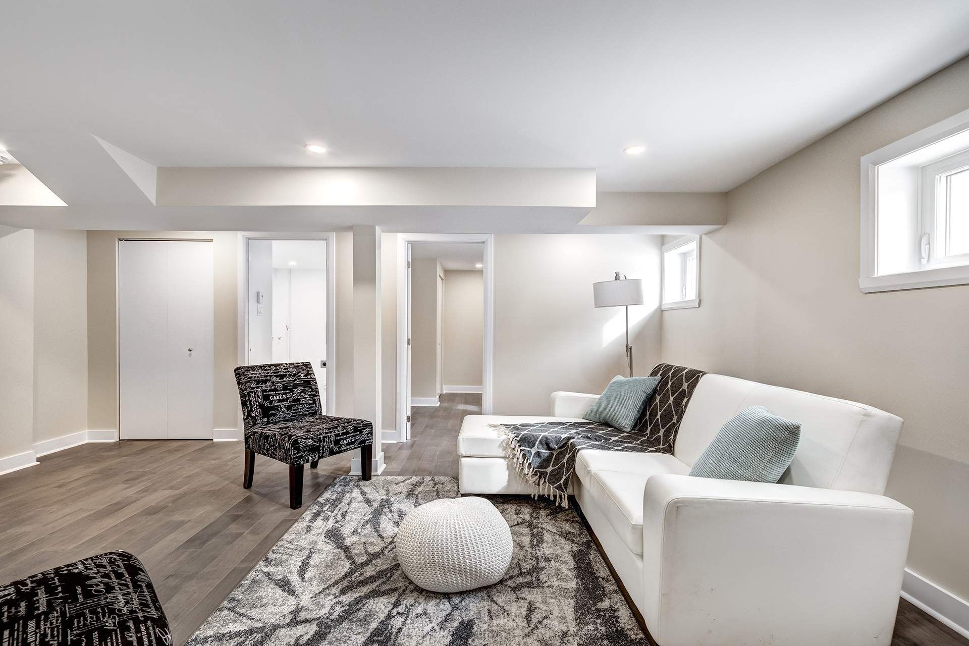 Cozy living room with white sectional, patterned rug, and accent chair. Neutral walls and hardwood flooring.