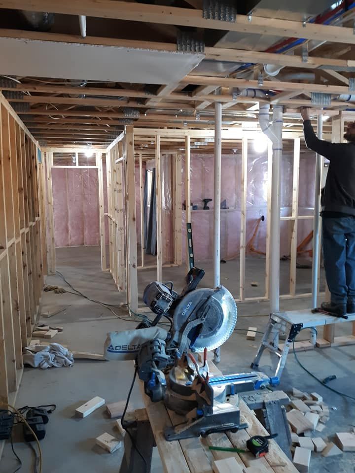 Construction site with a man working on plumbing. Saw is in the foreground, wooden frames and pink insulation are visible.