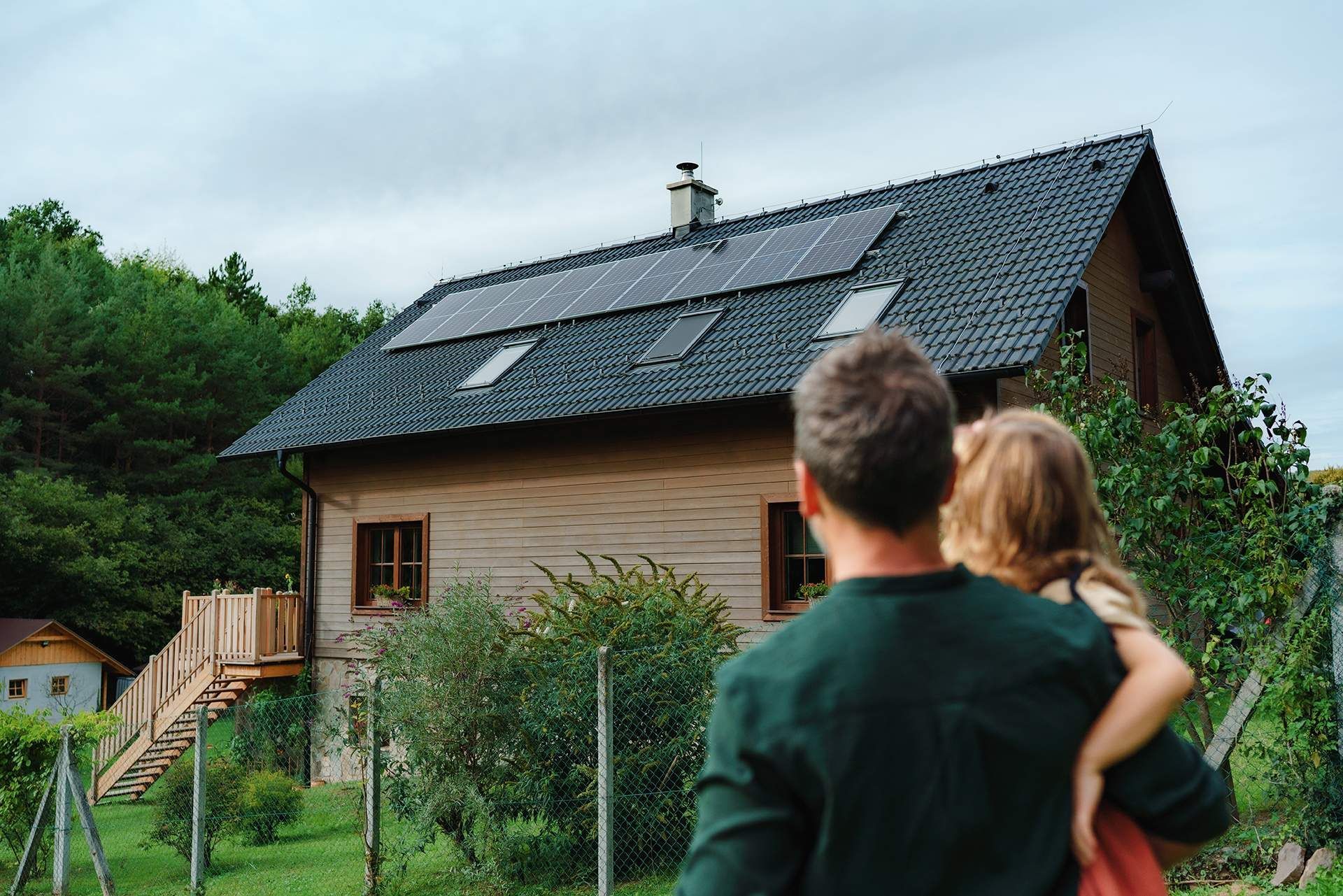 A man and a little girl are looking at a house with solar panels on the roof.