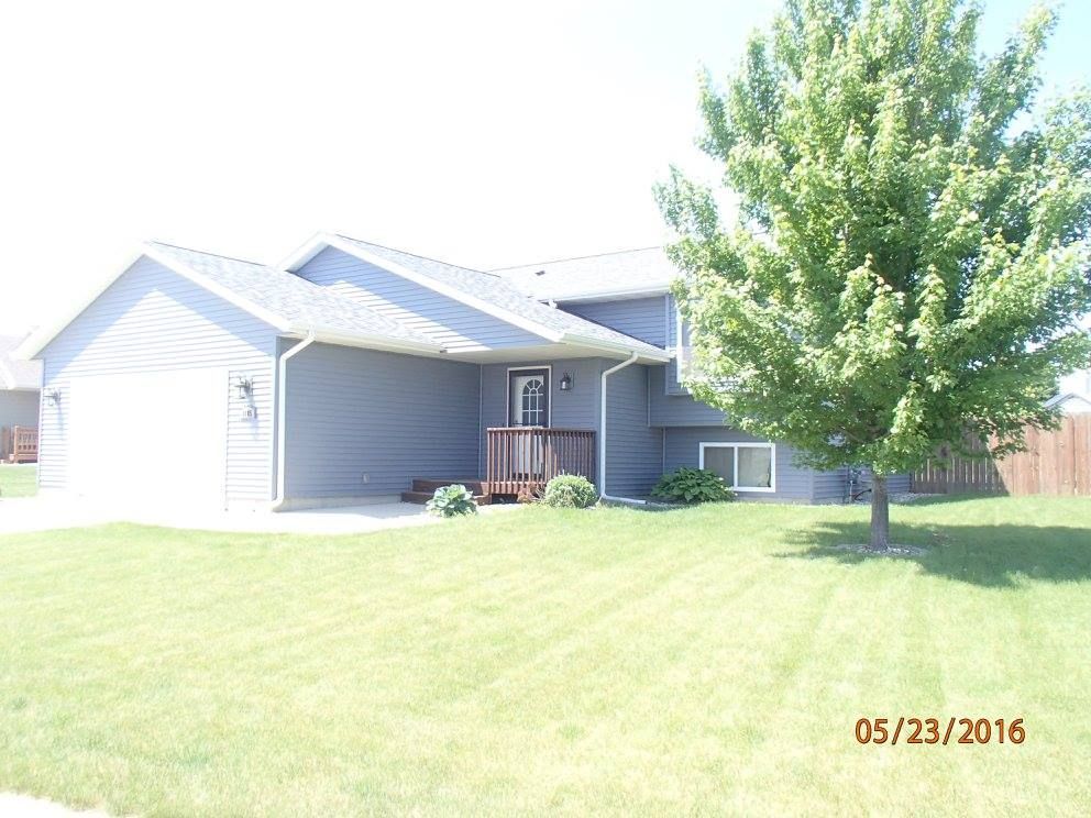 Blue house with attached garage, front porch, and large tree on a grassy lawn.